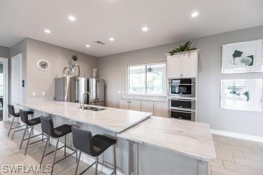 Kitchen with a breakfast bar area, recessed lighting, freestanding refrigerator, white cabinetry, and light stone countertops