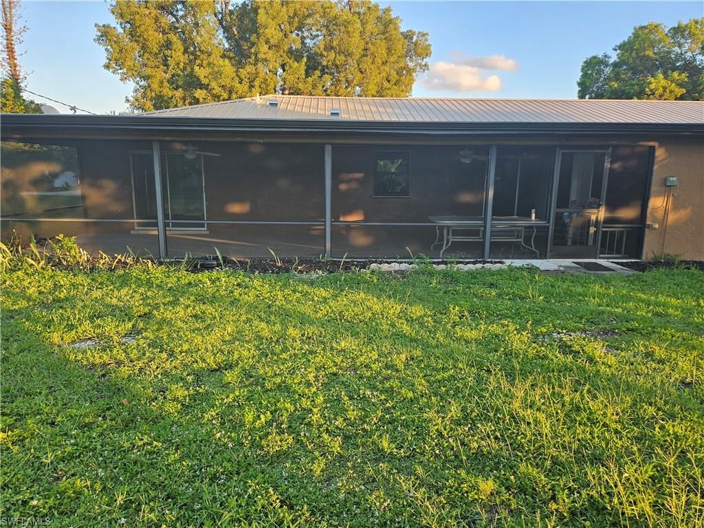 Rear view of house featuring a metal roof, a sunroom, a yard, and a ceiling fan
