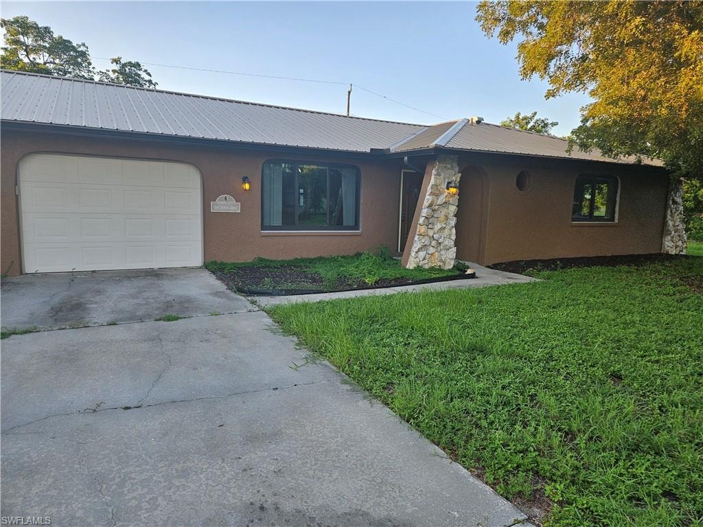 Ranch-style home with stucco siding, driveway, a metal roof, and a front lawn