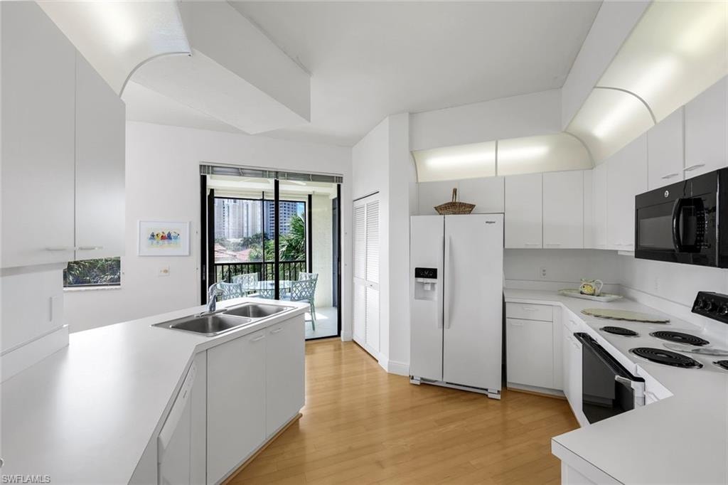 Kitchen with white appliances, light countertops, a peninsula, light wood-type flooring, and white cabinets