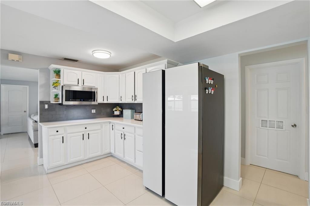 Kitchen featuring light tile patterned floors, freestanding refrigerator, light countertops, white cabinets, and open shelves