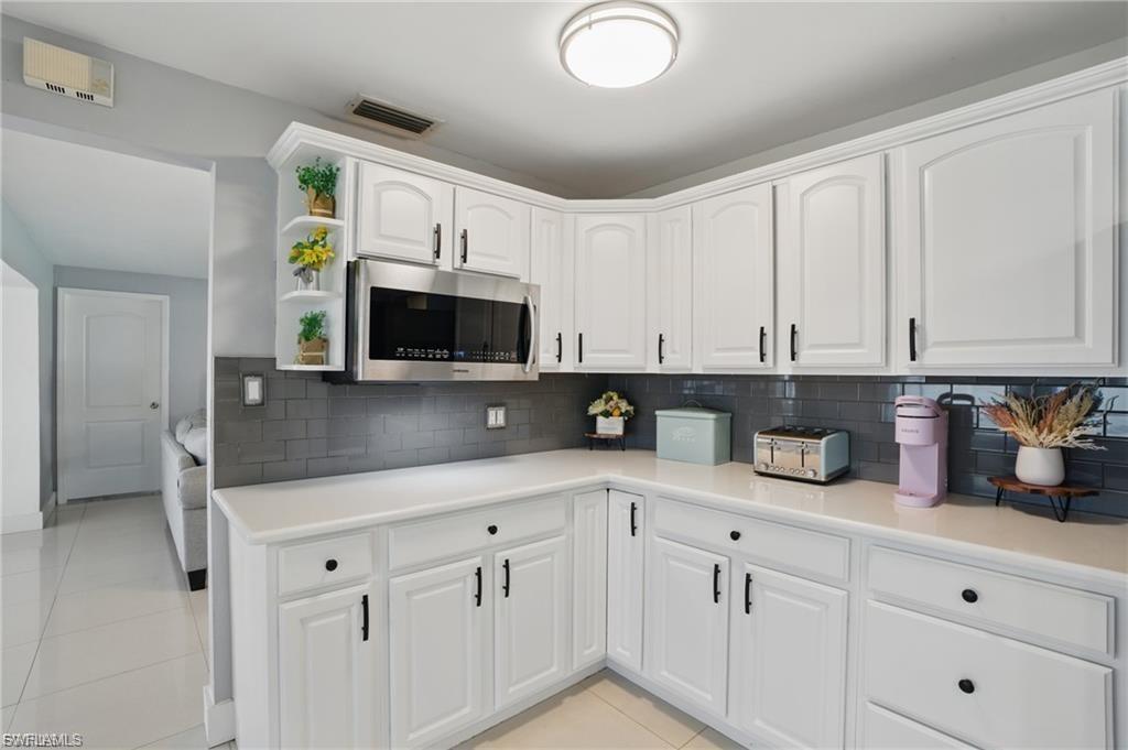 Kitchen featuring light countertops, white cabinets, light tile patterned floors, stainless steel microwave, and backsplash
