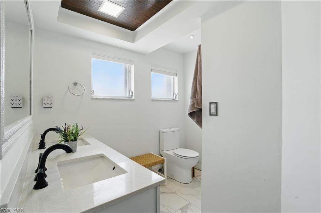 Full bathroom with double vanity, light marble finish floors, and a tray ceiling
