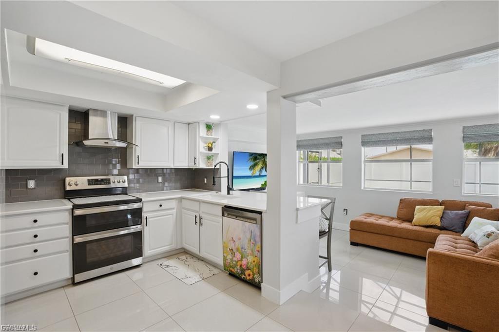 Kitchen with appliances with stainless steel finishes, open floor plan, wall chimney exhaust hood, white cabinetry, and recessed lighting