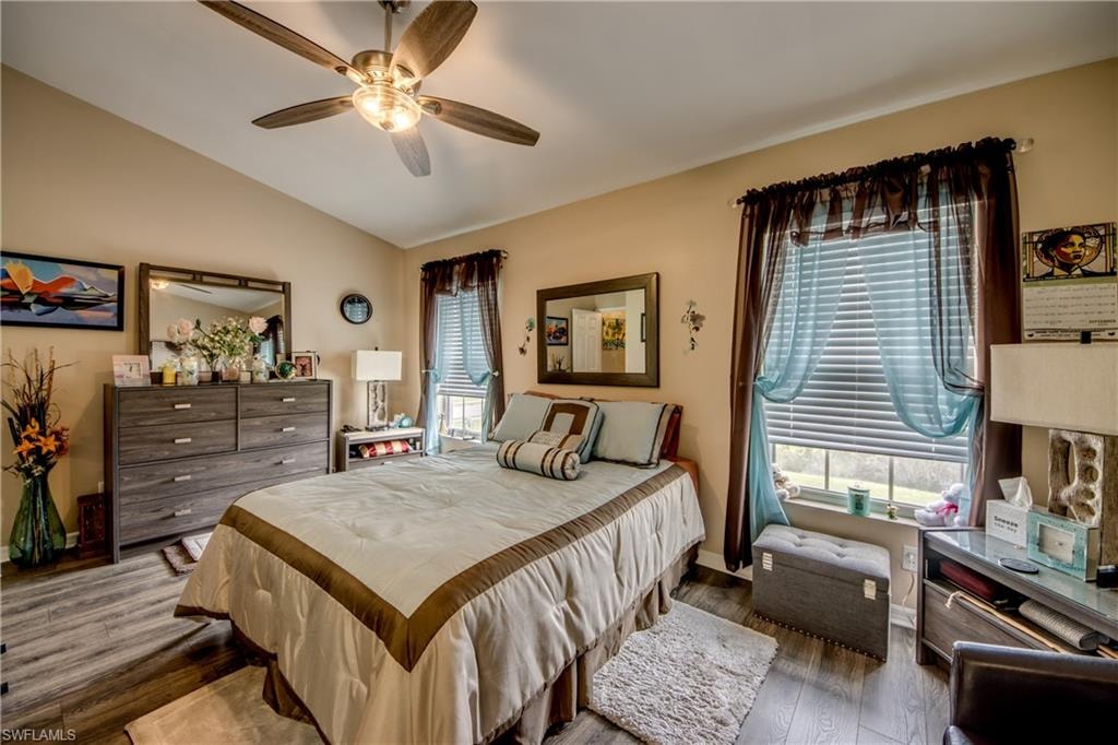 Master bedroom with dark wood-style floors, vaulted ceiling, and a ceiling fan