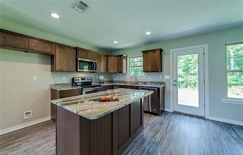 Kitchen with light stone countertops, stainless steel appliances, recessed lighting, dark brown cabinets, and a kitchen island