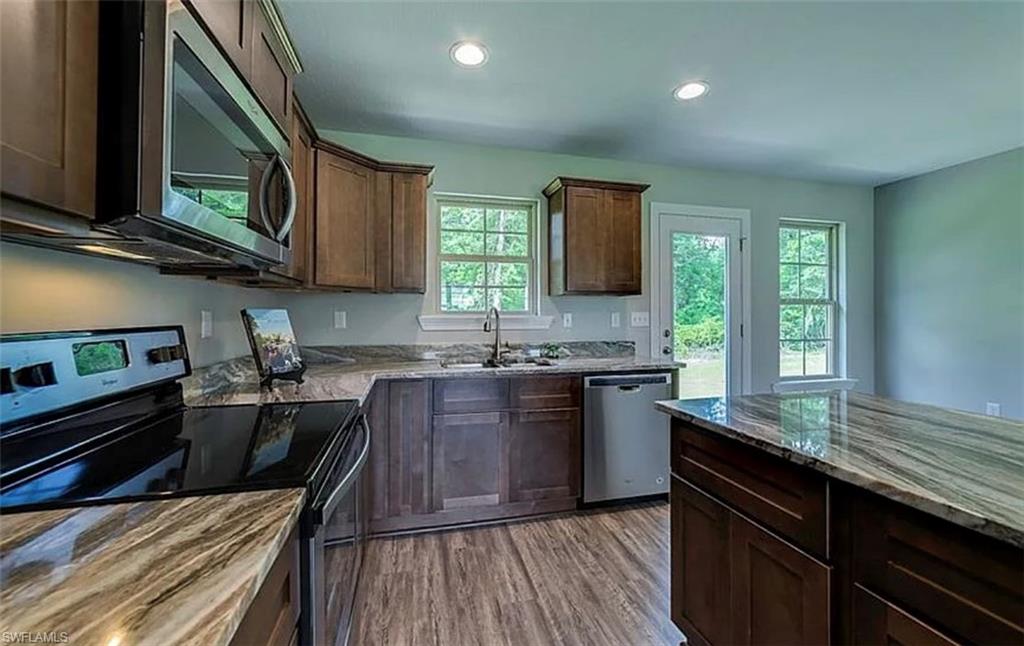 Kitchen featuring stainless steel appliances, dark wood-style flooring, dark brown cabinetry, recessed lighting, and dark stone countertops