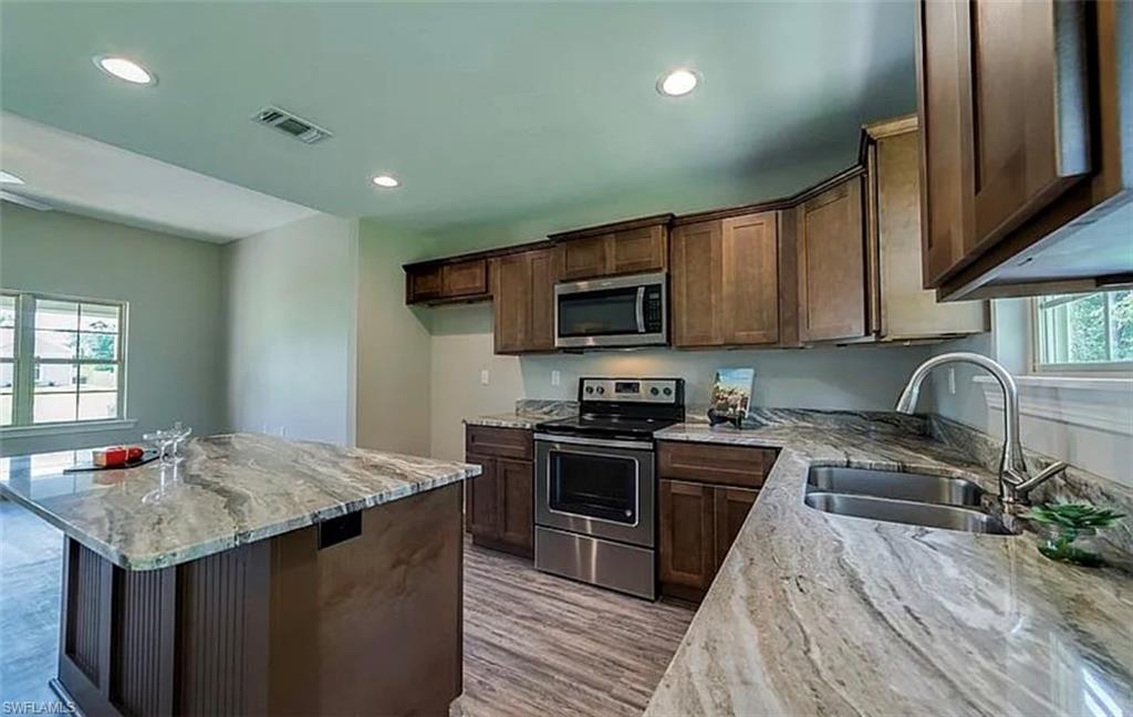 Kitchen featuring light stone countertops, stainless steel appliances, dark brown cabinetry, light wood-style floors, and recessed lighting