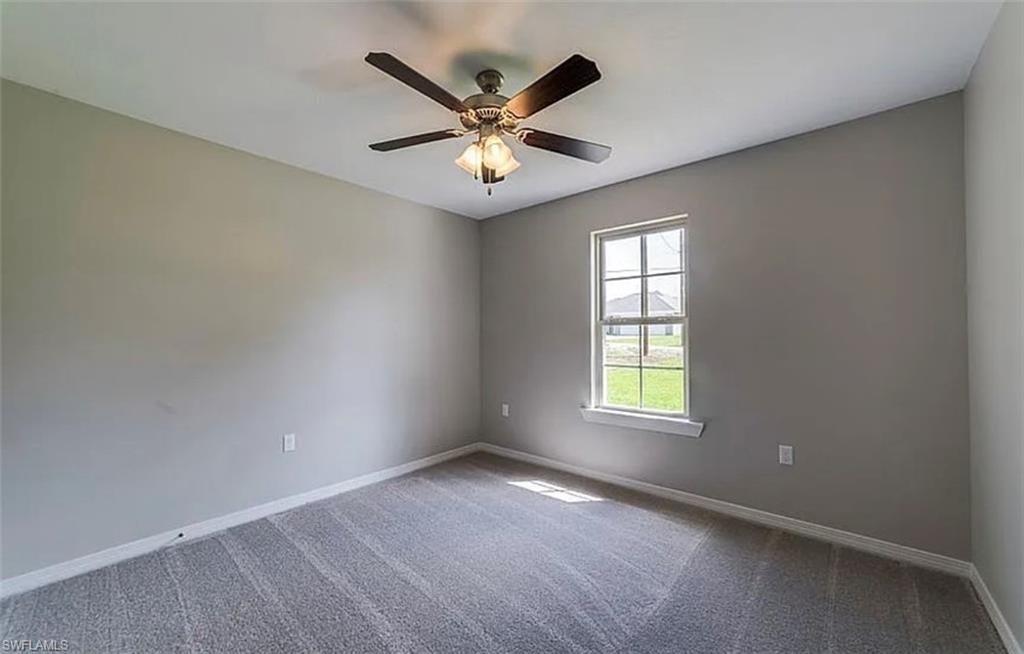 Carpeted empty room featuring baseboards and a ceiling fan
