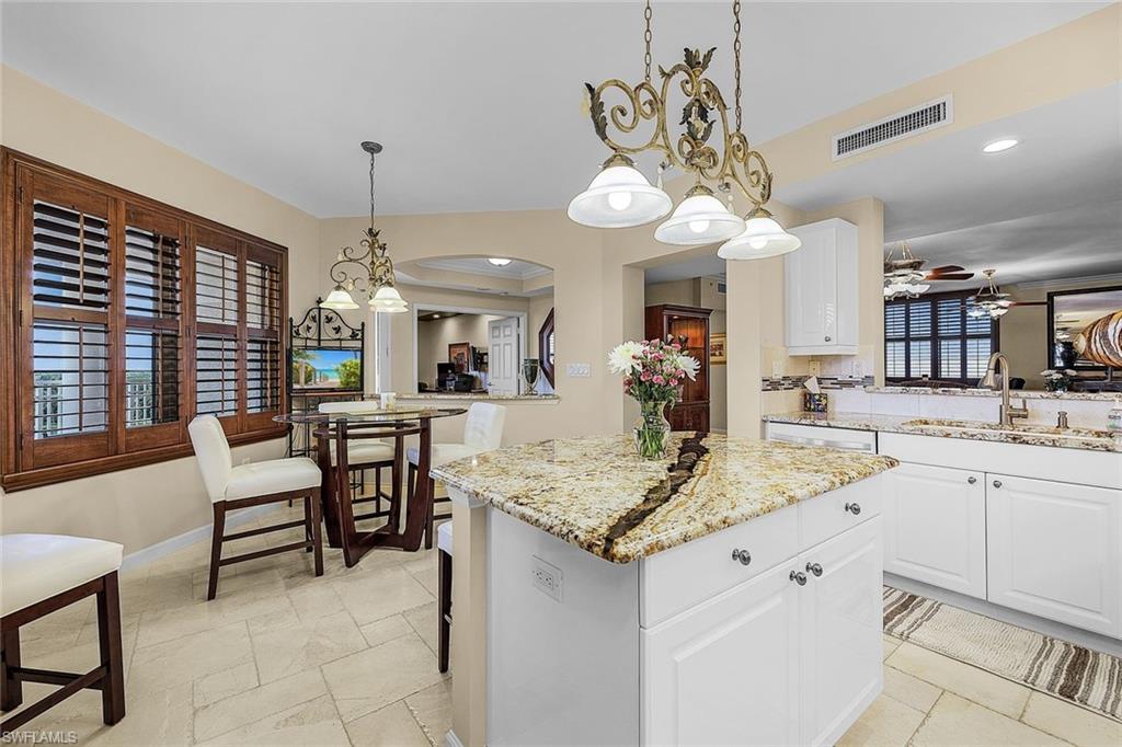 Kitchen with white cabinets, a kitchen island, decorative light fixtures, light stone counters, and recessed lighting