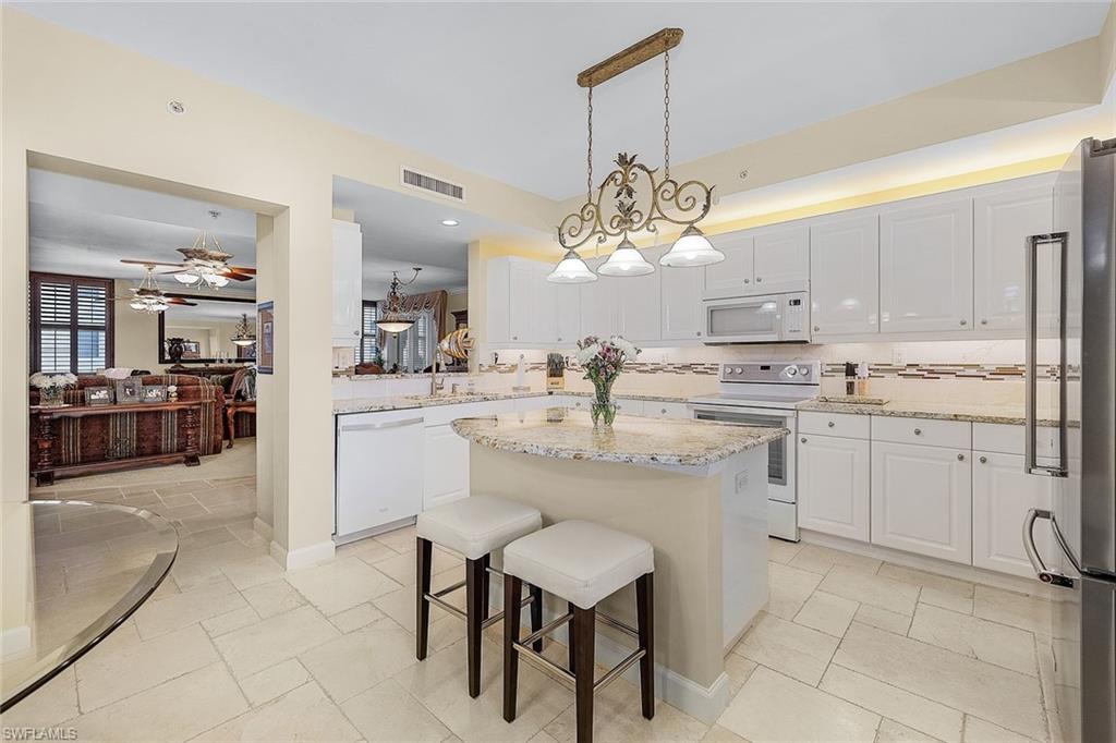 Kitchen with decorative light fixtures, a breakfast bar, white appliances, light stone countertops, and a kitchen island