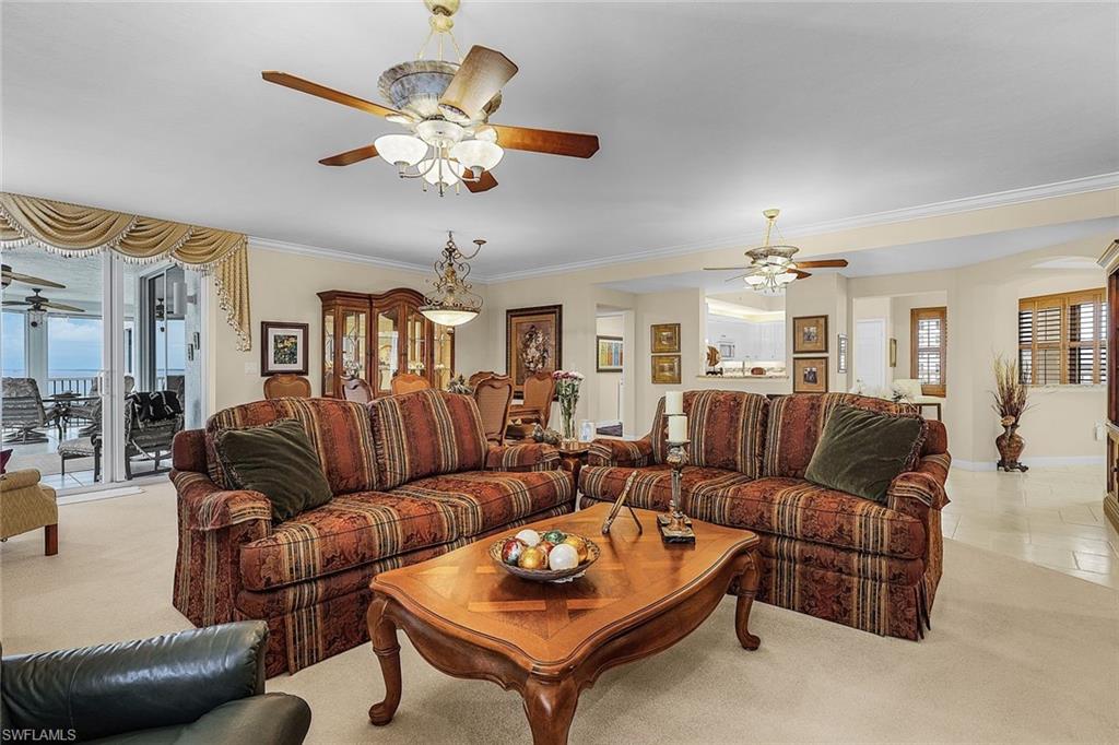 Living room with a ceiling fan, light carpet, crown molding, and light tile patterned flooring