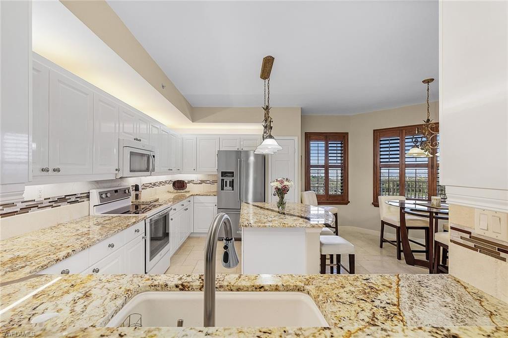 Kitchen featuring backsplash, pendant lighting, white appliances, white cabinets, and light stone counters