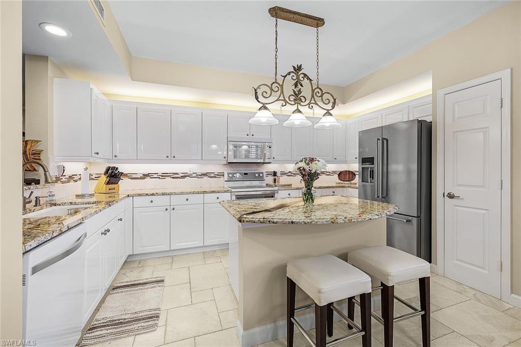Kitchen featuring a breakfast bar, a center island, light stone countertops, stainless steel appliances, and hanging light fixtures