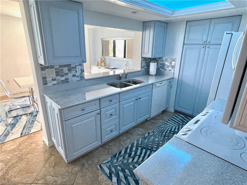 Kitchen featuring decorative backsplash, white appliances, light stone countertops, and a raised ceiling
