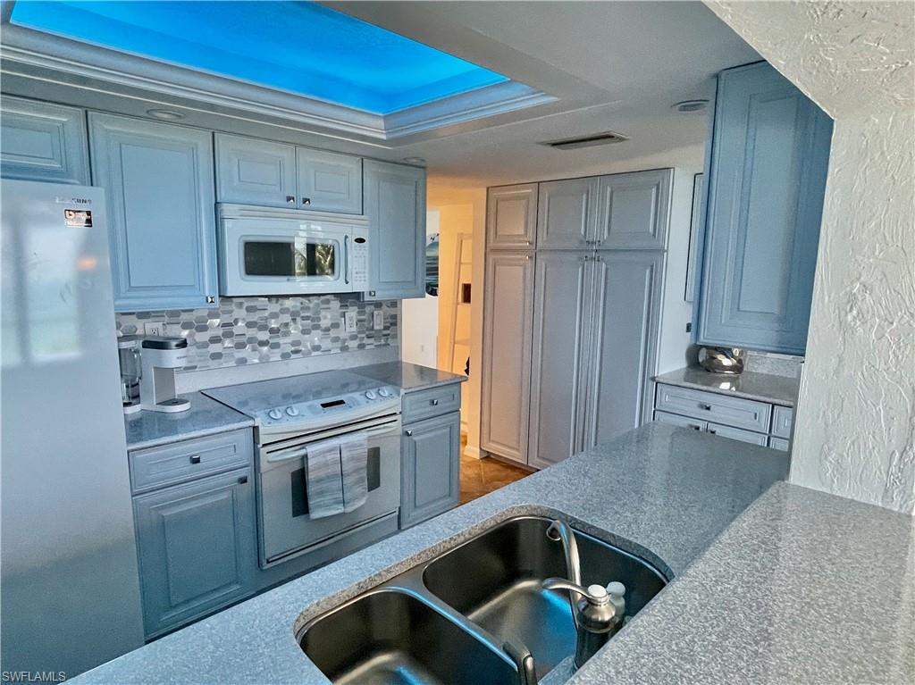 Kitchen featuring white appliances, a textured wall, decorative backsplash, light countertops, and gray cabinets