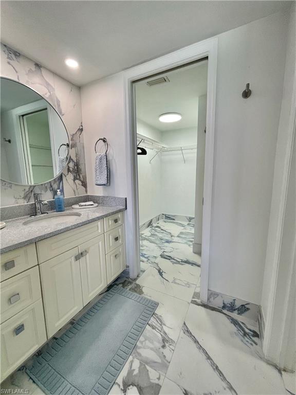 Bathroom featuring a walk in closet, light marble finish floors, vanity, and recessed lighting