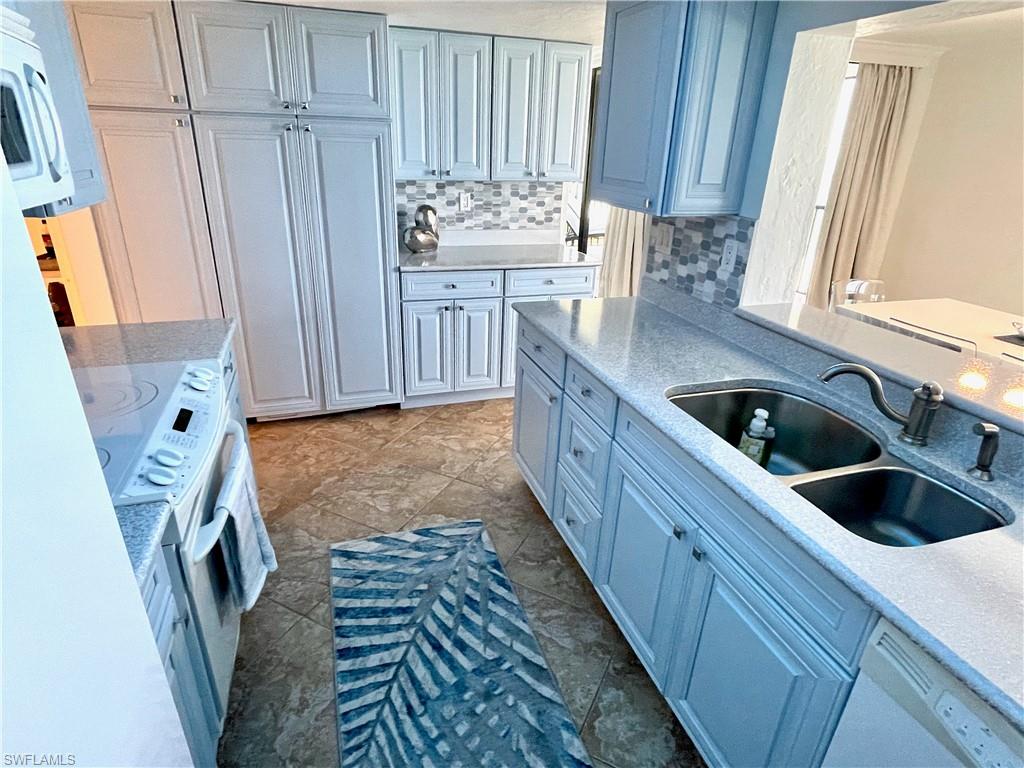 Kitchen with light stone countertops, white appliances, decorative backsplash, and light tile patterned flooring
