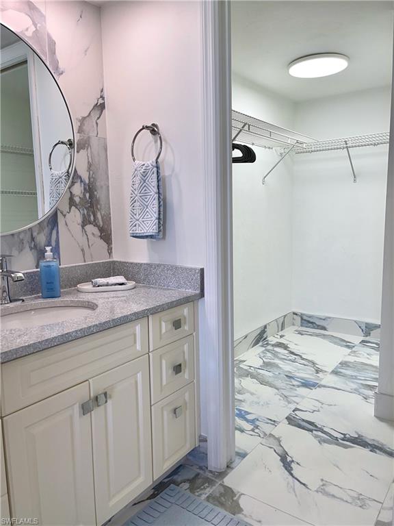 Full bath with light marble finish floors, vanity, and a walk in closet