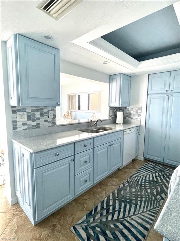 Kitchen with a raised ceiling, backsplash, blue cabinets, white dishwasher, and dark tile patterned flooring