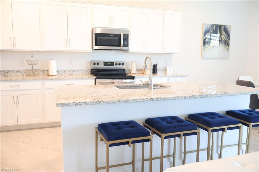 Kitchen featuring a kitchen breakfast bar, light stone counters, stainless steel appliances, white cabinets, and an island with sink