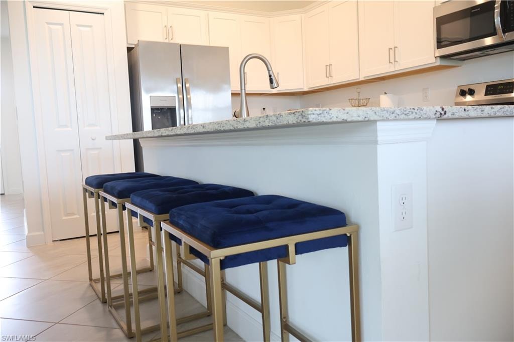 Kitchen featuring stainless steel appliances, white cabinetry, light tile patterned floors, light stone counters, and a breakfast bar
