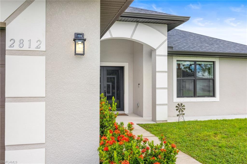 Property entrance featuring roof with shingles, stucco siding, and a lawn