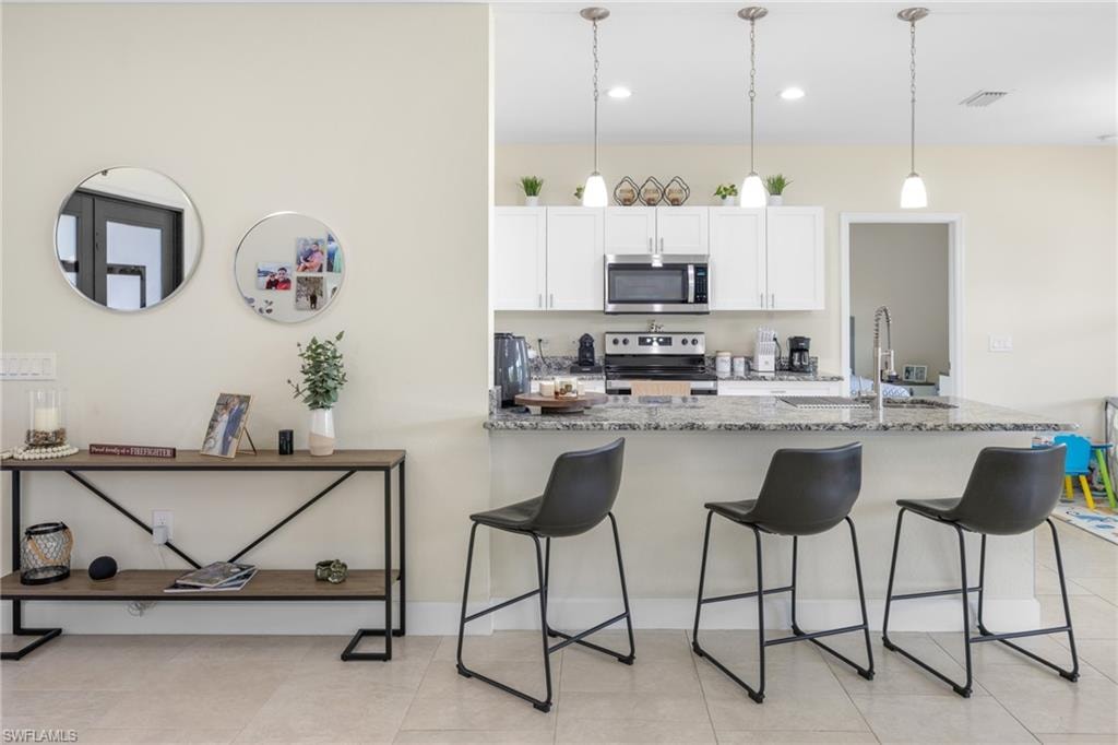 Kitchen with white cabinets, appliances with stainless steel finishes, hanging light fixtures, light tile patterned flooring, and a breakfast bar area