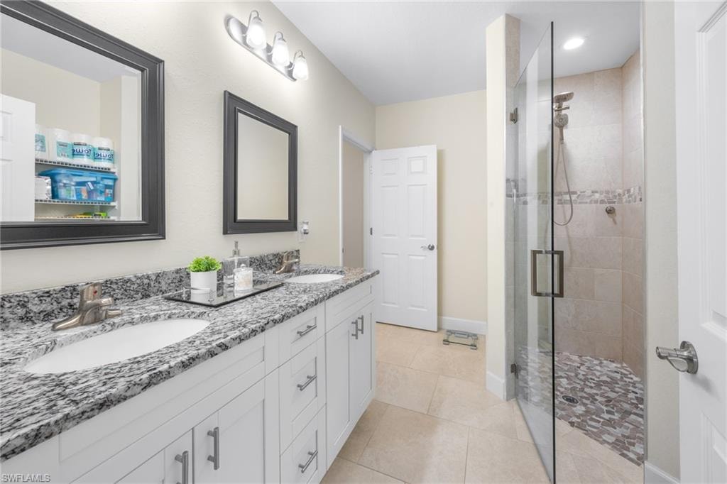 Bathroom featuring double vanity, a stall shower, and light tile patterned flooring