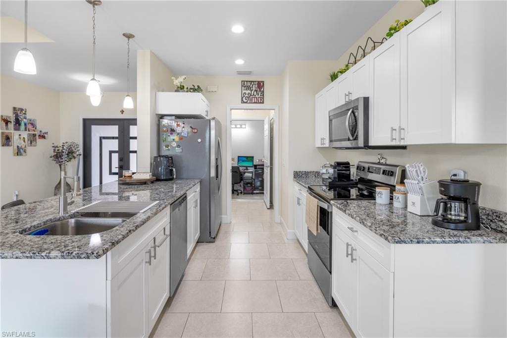 Kitchen with appliances with stainless steel finishes, white cabinets, light stone counters, hanging light fixtures, and light tile patterned flooring