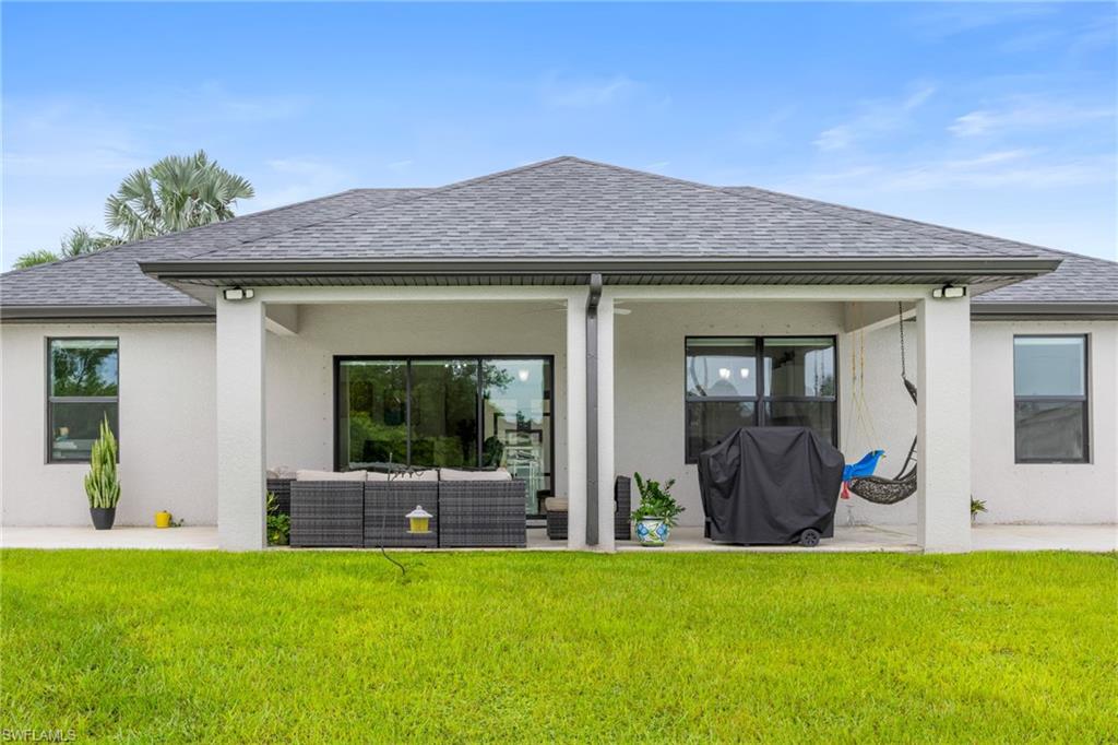 Rear view of house featuring a shingled roof, a patio, stucco siding, and a lawn