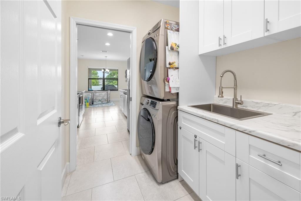 Laundry area with cabinet space, light tile patterned flooring, estacked washer and dryer, and recessed lighting