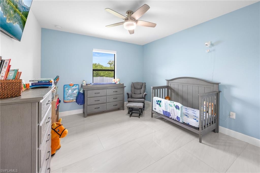 Bedroom with a nursery area, light tile patterned flooring, and ceiling fan