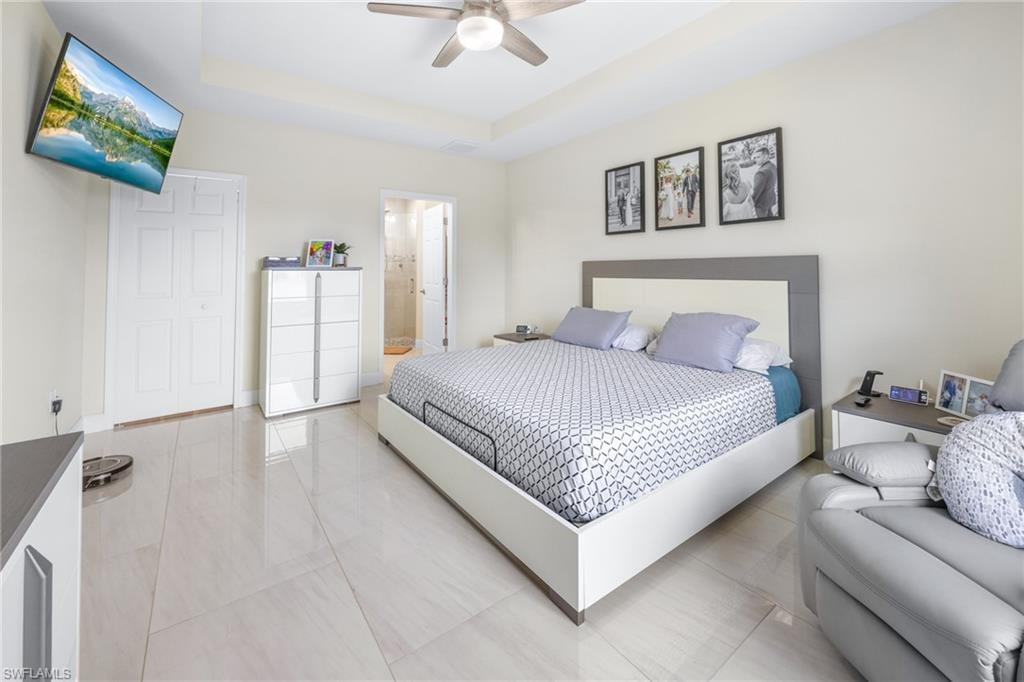 Tiled bedroom featuring a tray ceiling, ceiling fan, and ensuite bathroom