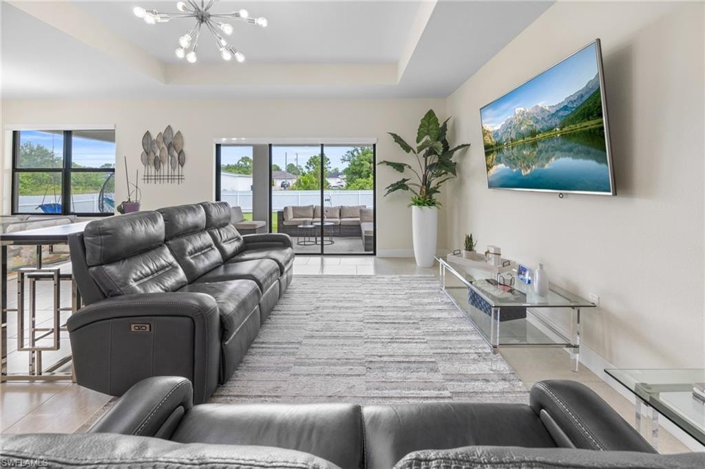 Living room featuring a tray ceiling, a chandelier, and light tile patterned flooring