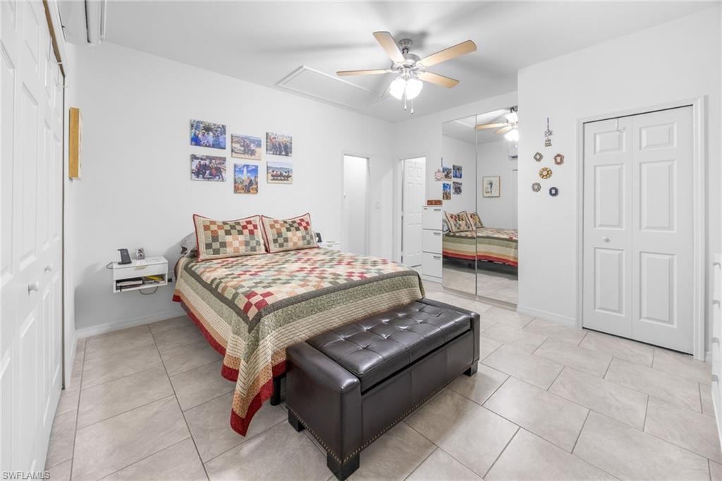 Bedroom with ceiling fan, attic access, light tile patterned flooring, and a wall mounted air conditioner