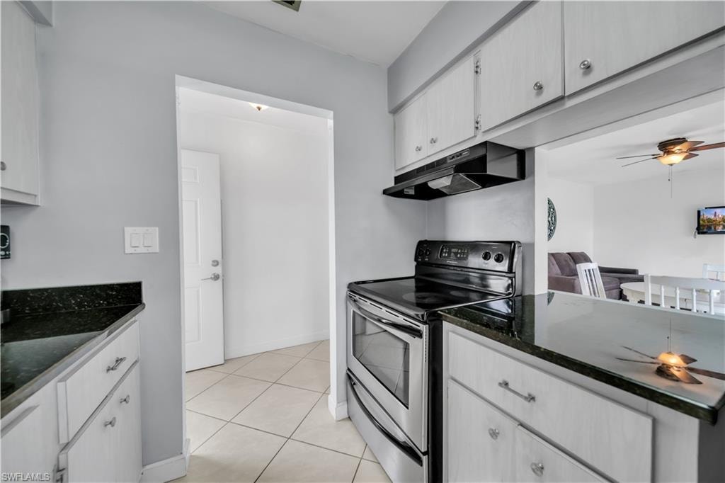 Kitchen with a ceiling fan, stainless steel range with electric cooktop, under cabinet range hood, dark stone countertops, and white cabinetry