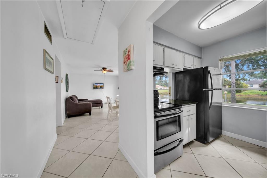 Kitchen featuring stainless steel electric stove, light tile patterned flooring, white cabinetry, and healthy amount of natural light