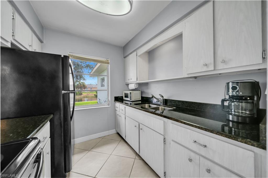 Kitchen featuring stainless steel range with electric stovetop, dark stone countertops, light tile patterned floors, freestanding refrigerator, and white cabinetry