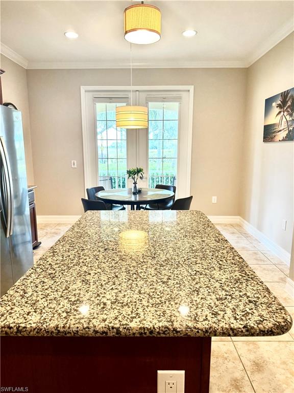 Kitchen island- stools coming, with freestanding refrigerator, ornamental molding, light stone counters, light tile patterned floors, and decorative light fixtures