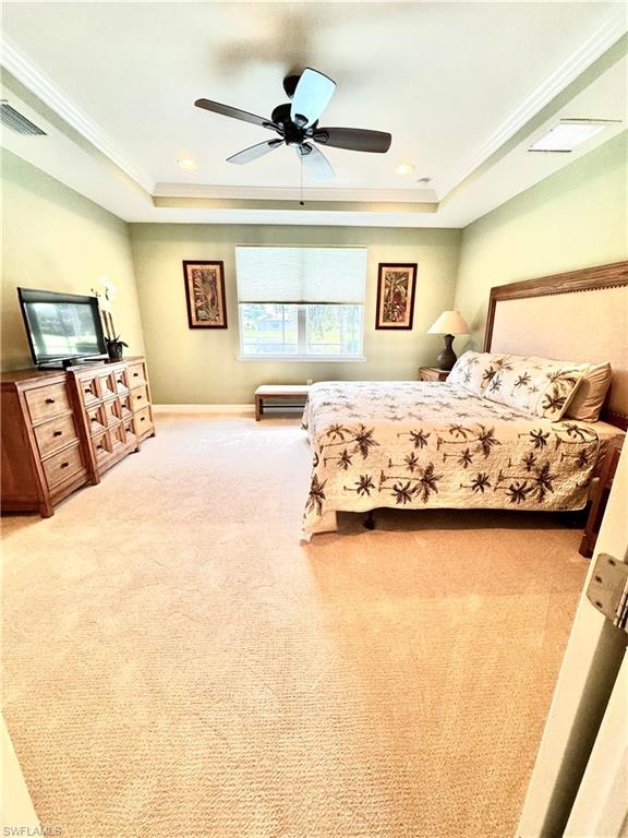 Bedroom featuring a tray ceiling, light carpet, ceiling fan, recessed lighting, and ornamental molding