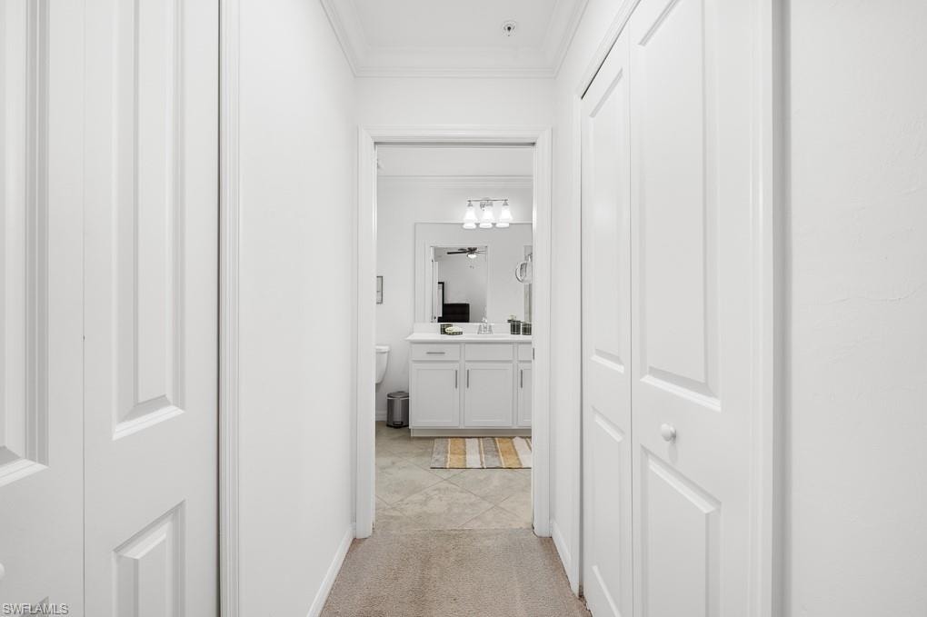 Corridor with ornamental molding, light carpet, and light tile patterned floors