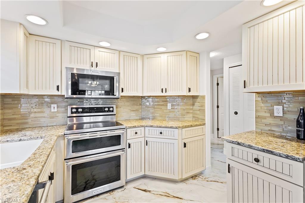 Kitchen with cream cabinetry, recessed lighting, light marble finish floors, appliances with stainless steel finishes, and light stone counters
