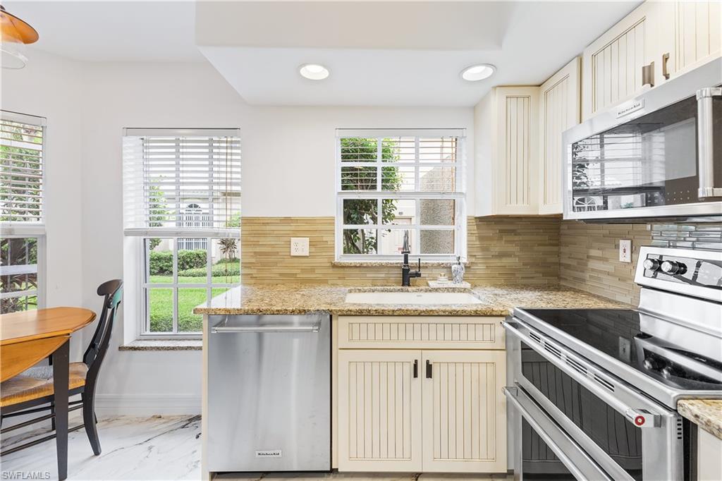 Kitchen featuring cream cabinetry, stainless steel appliances, decorative backsplash, recessed lighting, and light stone countertops
