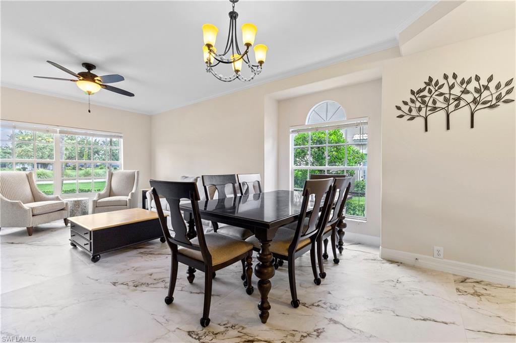 Dining space with ornamental molding, marble tiled floors, a chandelier, and a ceiling fan
