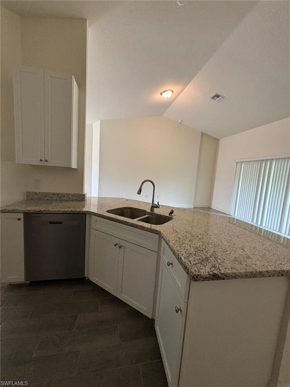 Kitchen with white cabinetry, a peninsula, dishwasher, light stone counters, and lofted ceiling