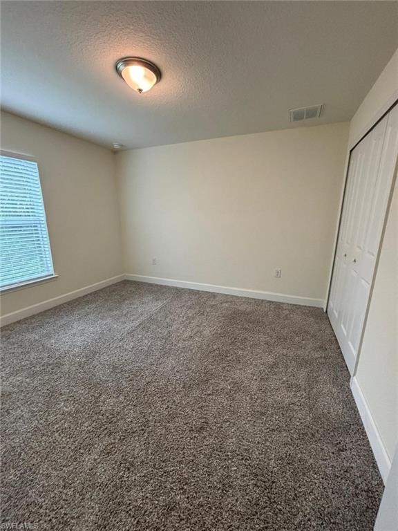 Unfurnished bedroom featuring dark carpet, a textured ceiling, and a closet