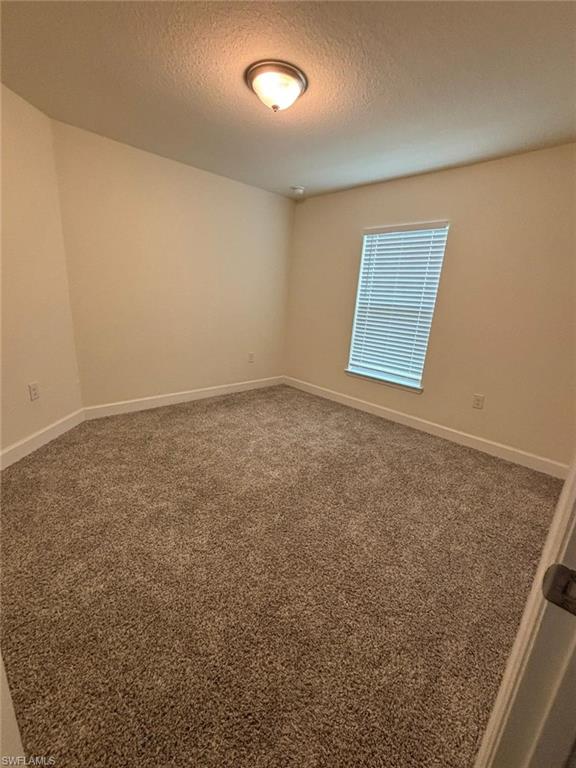 Carpeted spare room with a textured ceiling and baseboards
