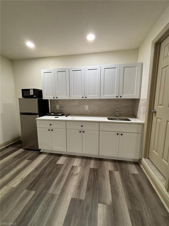 Kitchen featuring tasteful backsplash, white cabinetry, light countertops, dark wood-style floors, and recessed lighting