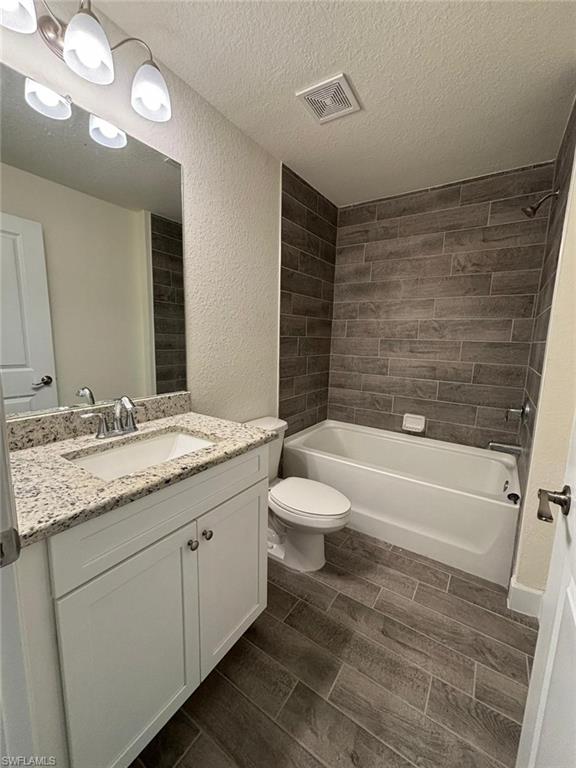 Full bathroom featuring wood tiled floors, shower / washtub combination, a textured ceiling, vanity, and a textured wall